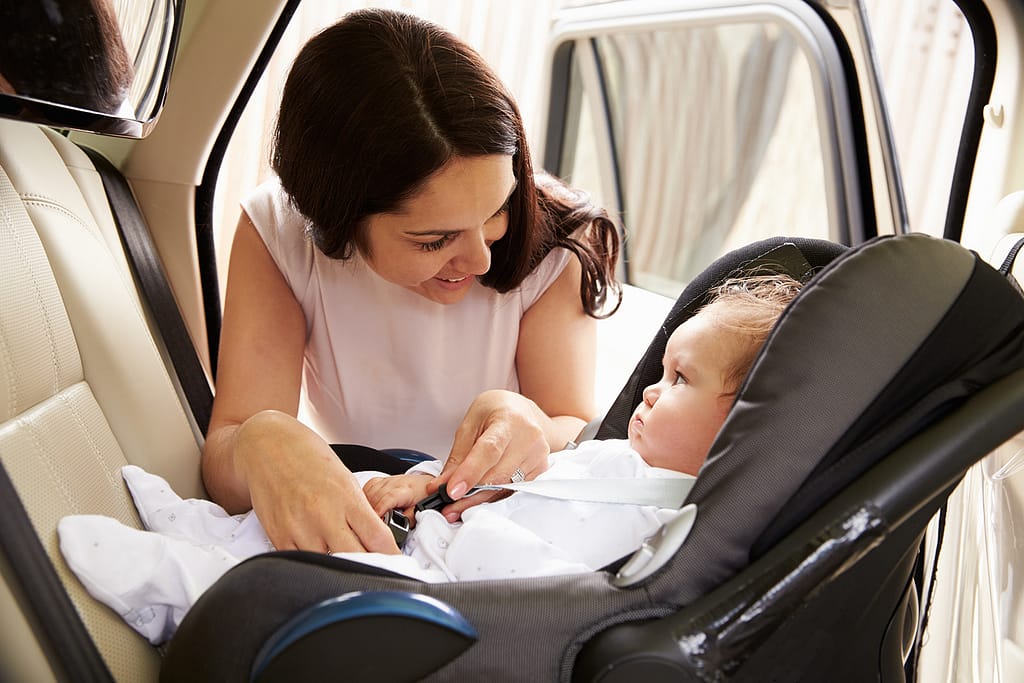 Woman buckling a child into a rear-facing car seat. Child Passenger Safety Laws by State (2024): Complete Guide