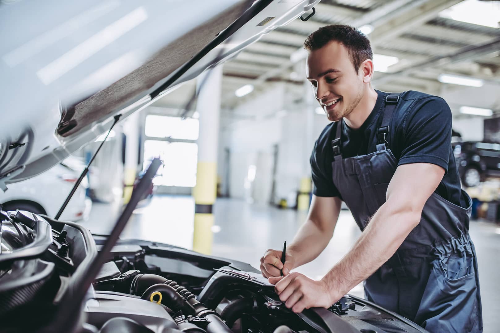 Handsome mechanic in uniform is examining the car while working in auto service. Car repair and maintenance. Texas Car inspection