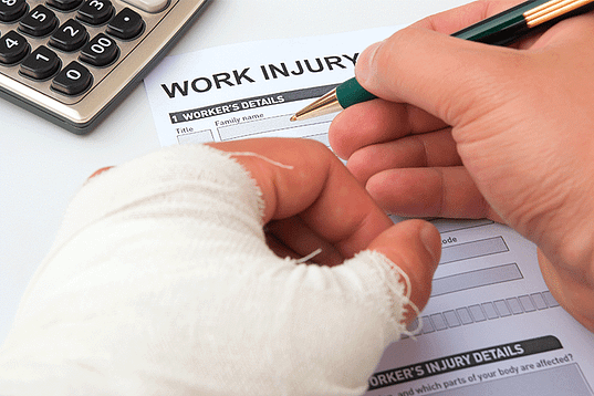 Man with bandaged hand filling out a work injury form - Workers compensation attorneys in Dallas Texas