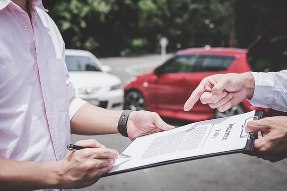 Man holding a clipboard while another man signs a document titled Insurance Policy - What is auto insurance subrogation in Texas?