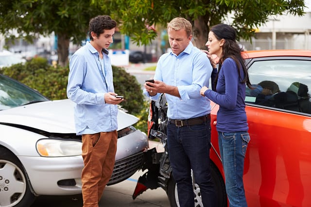 Teenager, woman and man, exchanging information after a car accident.