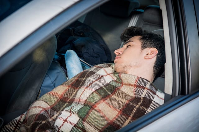 Young handsome man sleeping inside his car, exhausted, tired. Is it illegal to sleep in your car or live out of your car in Texas?