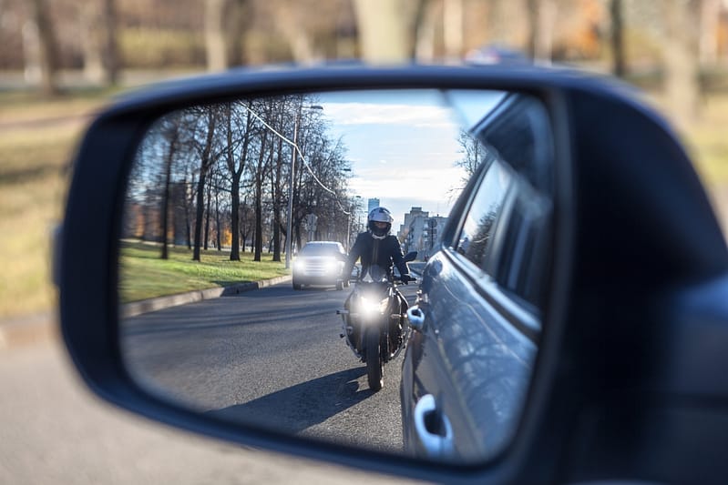 Mutual passing, motorcycle and vehicle with dazzle lighting overtaking the car, view in side mirror. Improper driving or traffic violation. Mesquite Motorcycle Accident