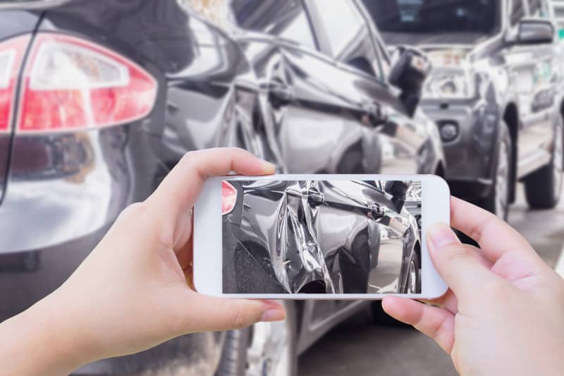Mujer tomando fotografías de daños a la propiedad de un automóvil después de un accidente automovilístico para fortalecer su reclamo por lesiones personales.
