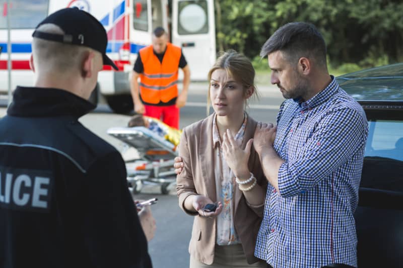 Una mujer es consolada por un hombre mientras hablan con la policía después de un accidente automovilístico. Tres maneras en que puede ayudar a fortalecer su caso de lesiones personales