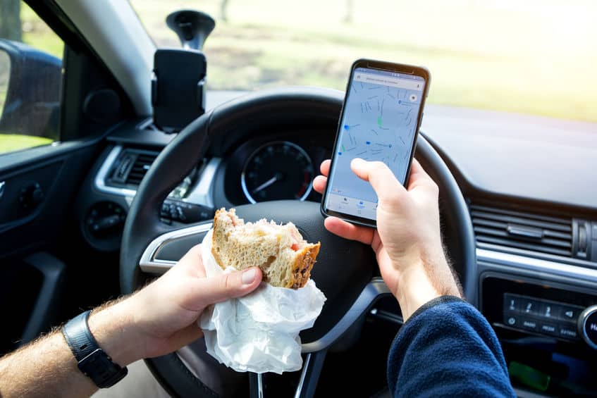 Distracted driving. man eating and texting while driving car